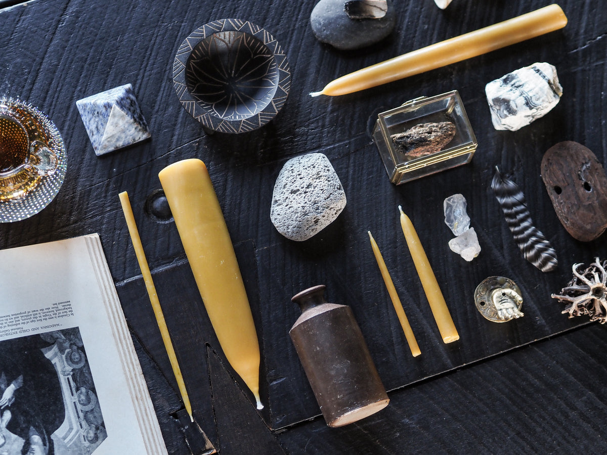 Collection of beeswax candles, stones, and natural curiosities on a dark wooden table
