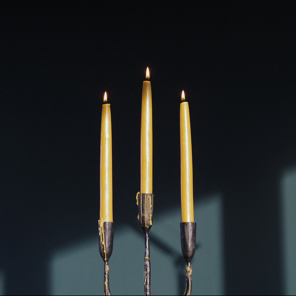 Three lit taper candles in dark iron holders against a very dark background with soft teal shadows.