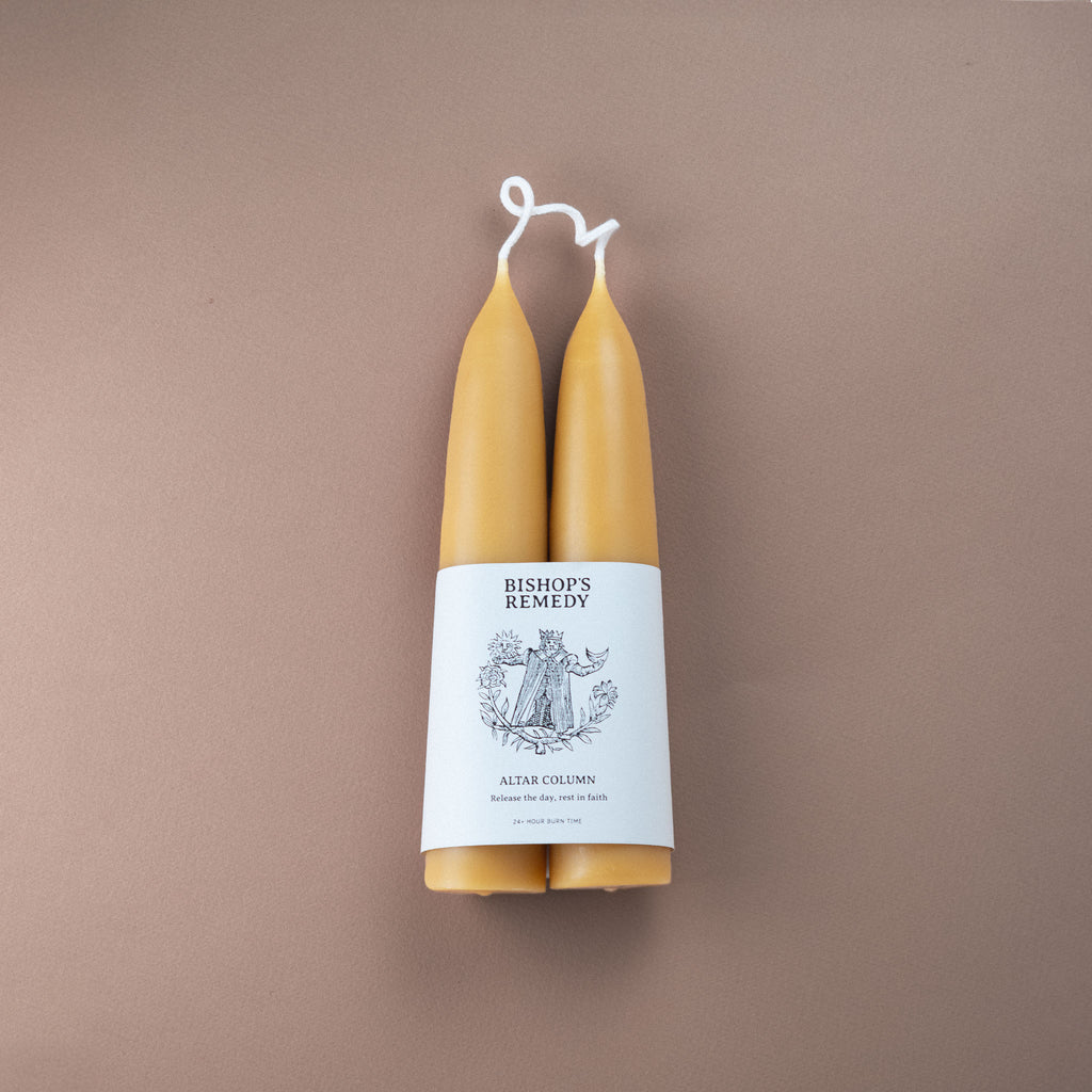 Two hand made beeswax candles with a white label on a brown background