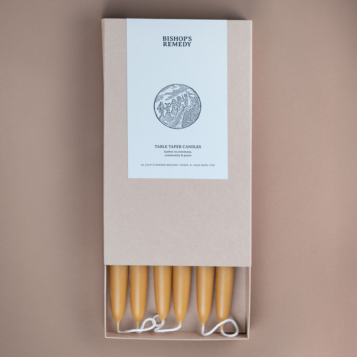 A boxed set of Bishop's Remedy table taper candles, shown from above on a warm taupe background. The product is in a light beige kraft paper box with a white label, and five pale yellow wax candles are visible at the bottom with white wicks.