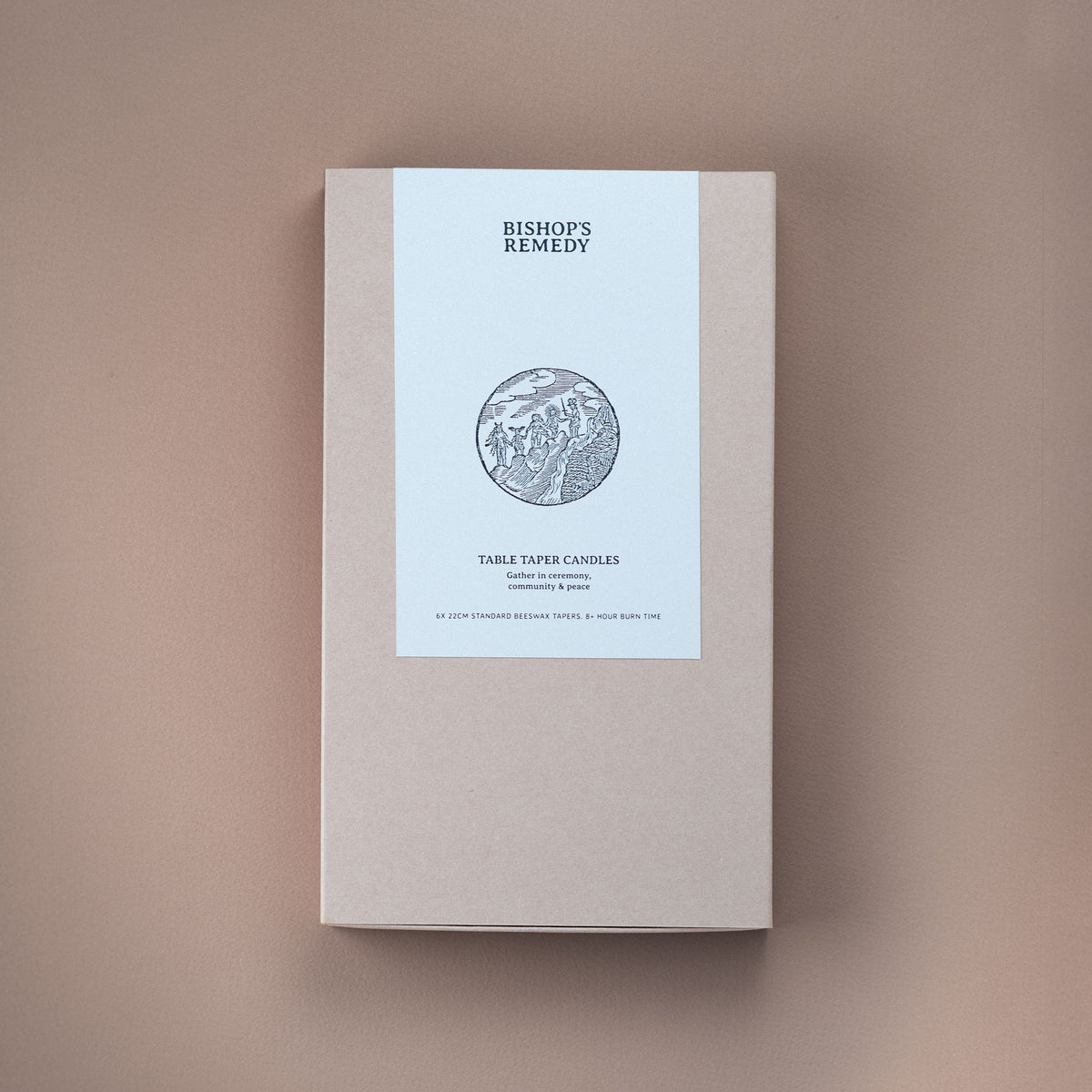 A rectangular beige product box with a white vertical label reading 'BISHOP'S REMEDY' and 'TABLE TAPER CANDLES' with a circular etched illustration, photographed on a warm taupe background.