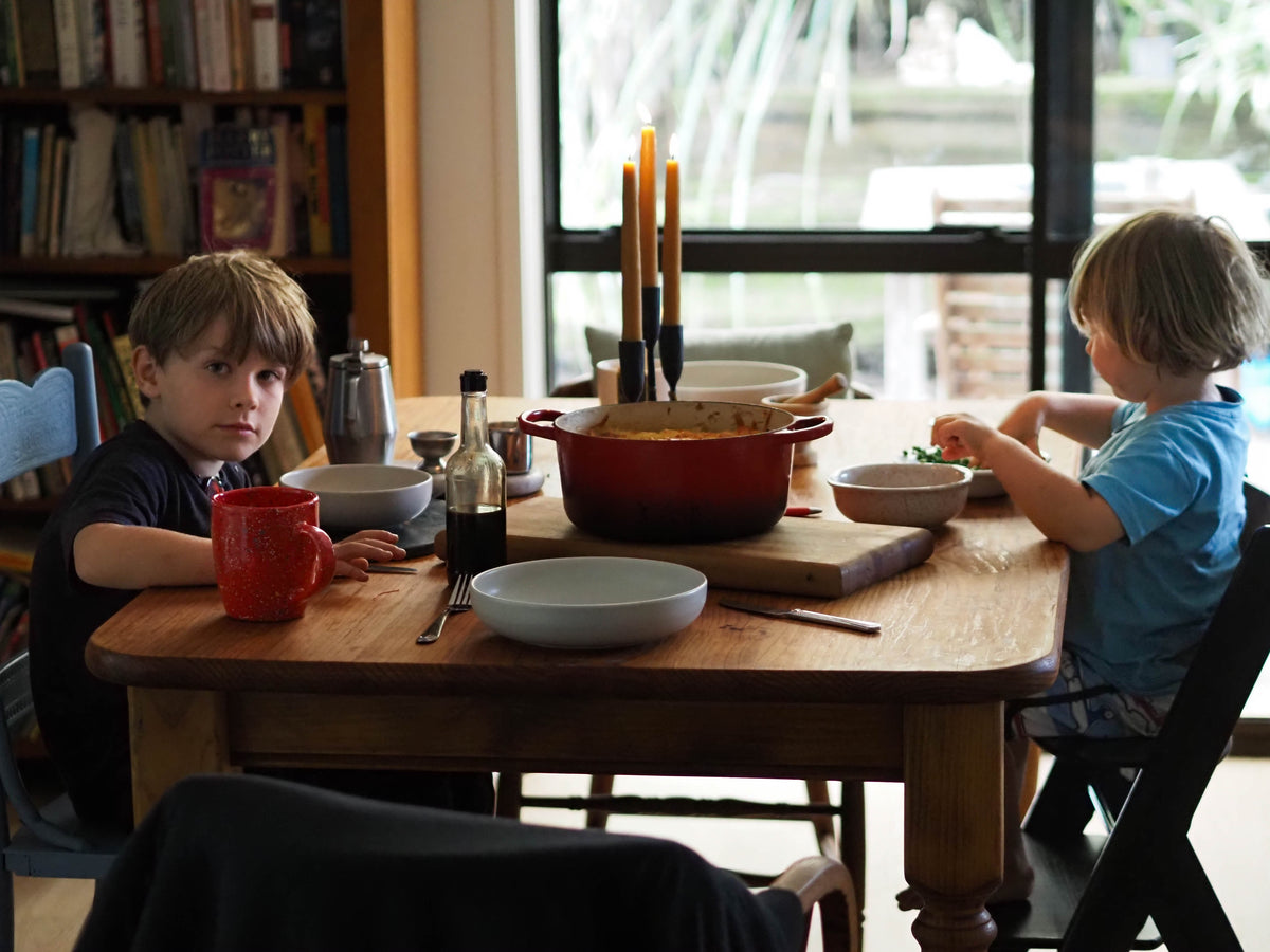 Two children sitting at a wooden table with various items including bowls and a candelabra.